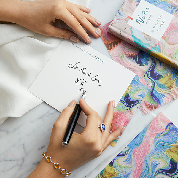 Women wearing a blue sapphire ring and writing a note card on stationary from Fenton x Papier.