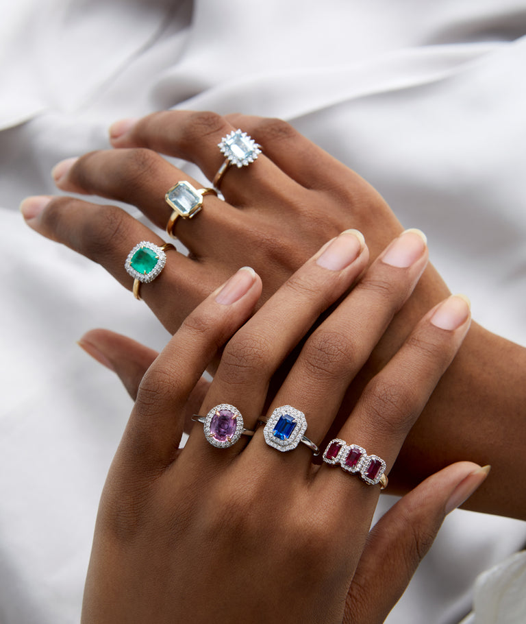 Two hands wearing a variety of gemstone rings